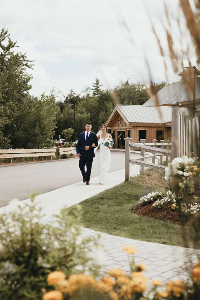 Bride and brother walking down sidewalk towards ceremony area.